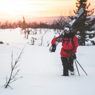 A skier walks through a snowy landscape in Sweden during a vibrant winter sunset.