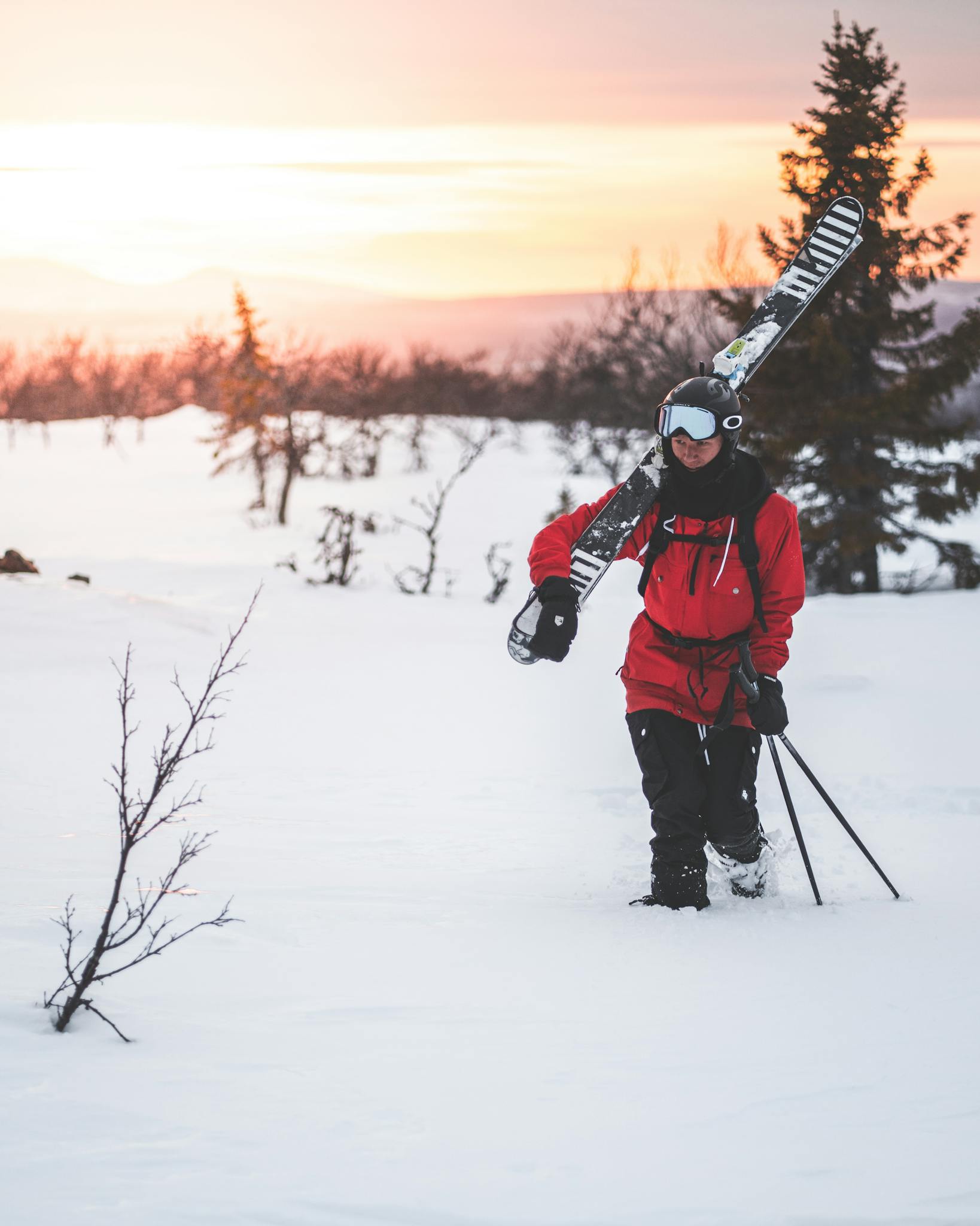 A skier walks through a snowy landscape in Sweden during a vibrant winter sunset.