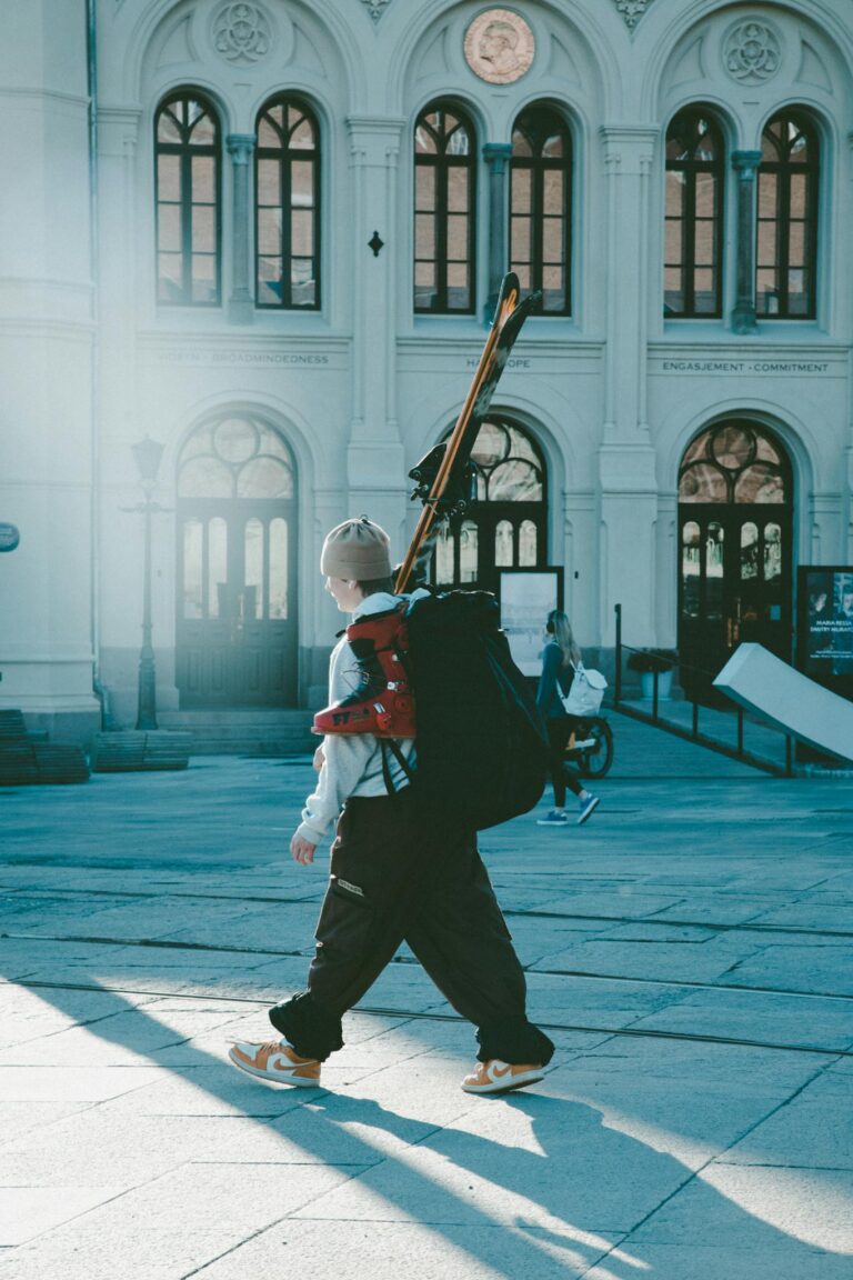 Man with skis walking through Oslo urban area on a sunny winter day.